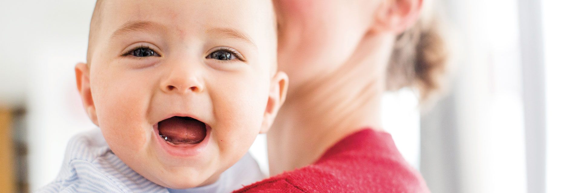 Foto: Ein Kleinstkind blickt mit strahlendem Lachen über die Schulter seiner Mutter.