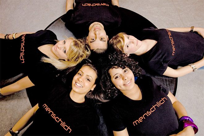 Foto: Fünf Jugendliche liegen Kopf an Kopf im Kreis. Sie lachen und wirken vergnügt und herzlich. Alle tragen ein schwarzes T-Shirt mit der Aufschrift 'menschlich'.