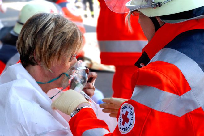 Foto: Bei einer Helferübung wird eine verletzte Person von einer DRK-Einsatzkraft betreut. Die Patientin hält eine Sauerstoffmaske vor ihr Gesicht.